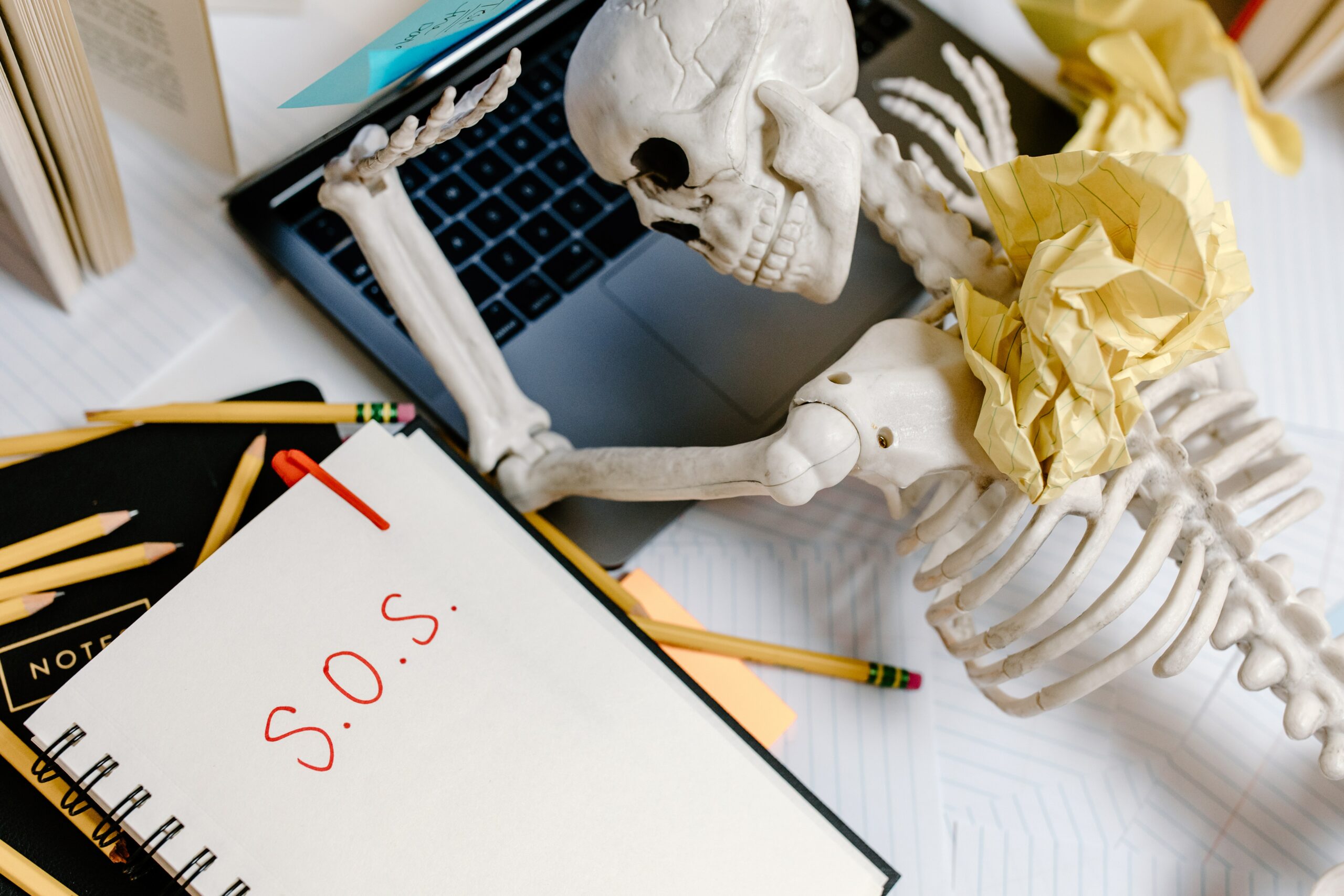 human skeleton on a laptop with a SOS letter next to it